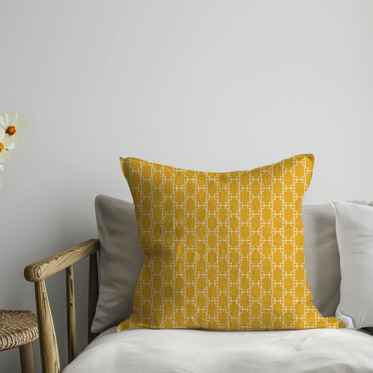 Yellow patterned pillow on a sofa next to a small table with flowers against a plain wall.